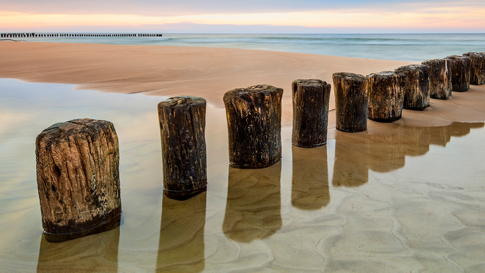 Wooden breakwaters on a sandy beach at sunrise