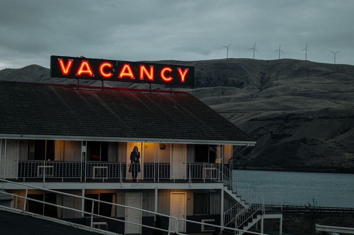 Motel with Vacancy neon sign and woman on balcony