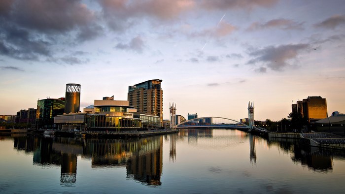 Manchester skyline with bridge and water reflection at sunset