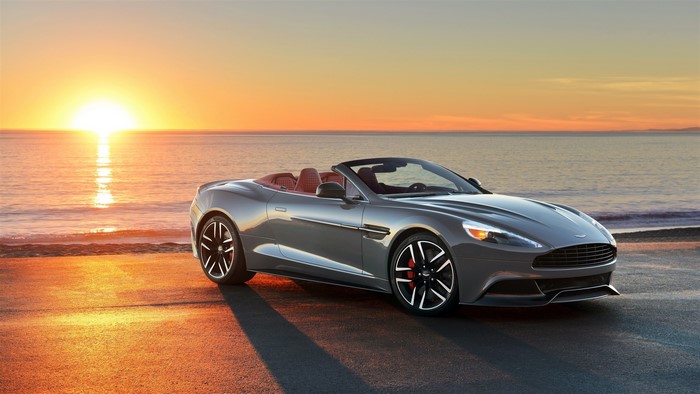 Silver Aston Martin convertible on a beach at sunrise