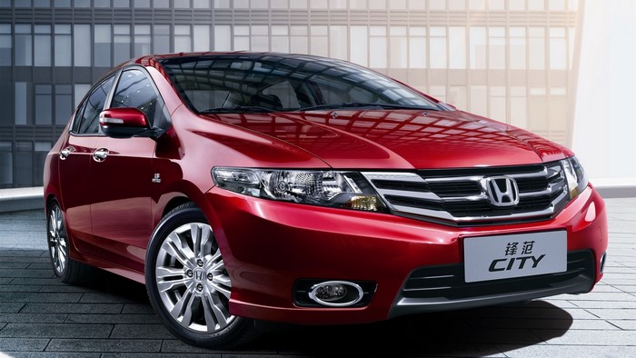Red Honda City car parked in front of a modern building
