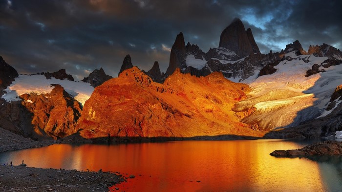 Mountain lake with rocky shore and snow-capped peaks at sunset