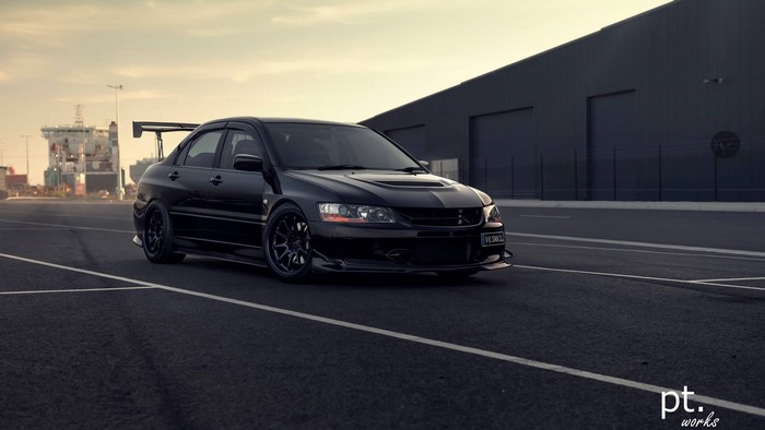 Black Mitsubishi Lancer EVO on asphalt near ships