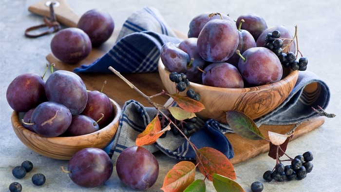 Plums and berries in wooden bowls with autumn leaves