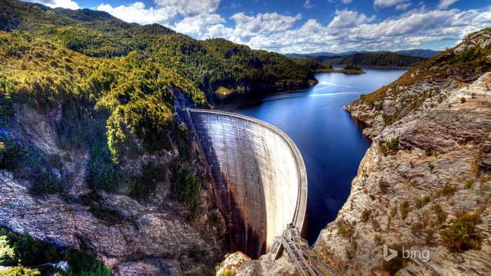 Curved concrete dam holding back a blue lake surrounded by forested mountains