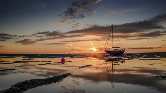 Red sailboat at sunset on a reflective tidal flat