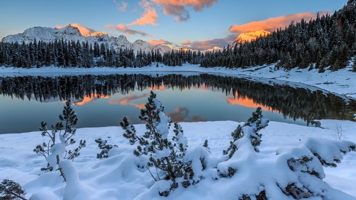 Snowy mountains and forest reflected in a calm lake at sunrise