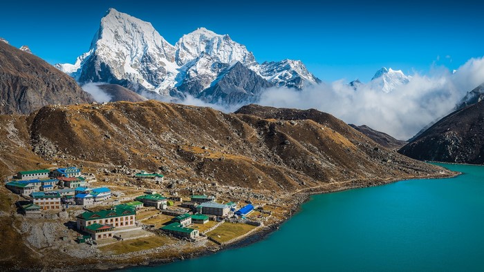 Village by turquoise lake with snowy Himalayas
