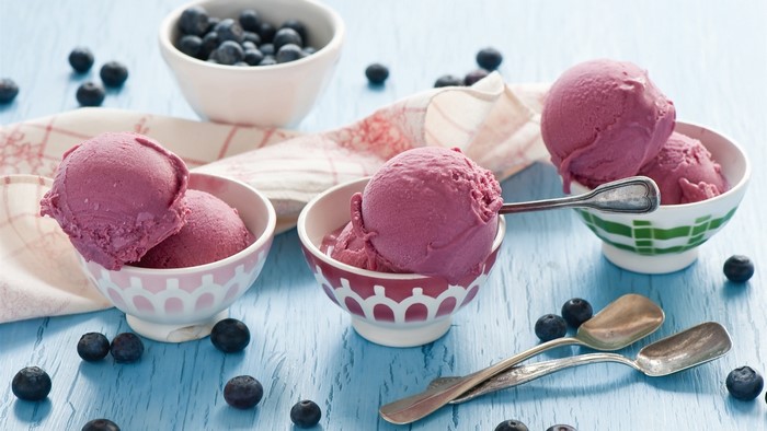 Blueberry ice cream in bowls with blueberries and spoons
