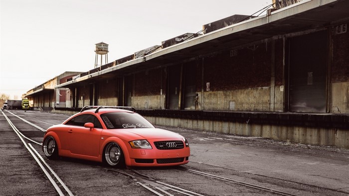 Red Audi TT parked on train tracks near warehouse
