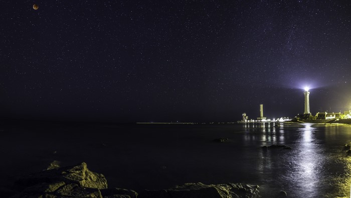 Lighthouse and moonlit sky over the sea