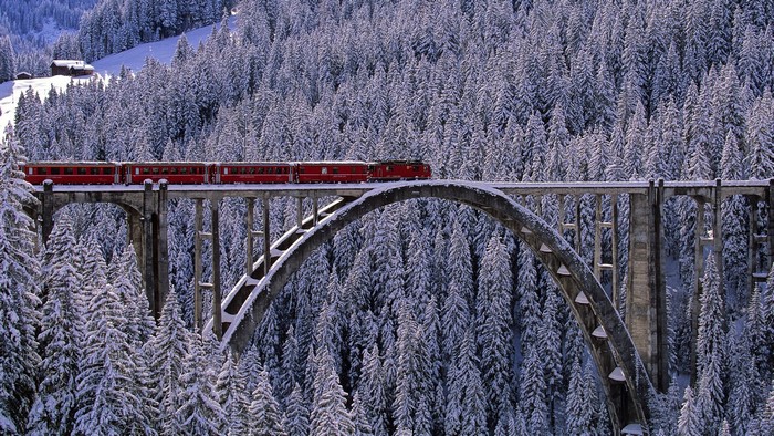 Red train on a snowy bridge in Arosa, Switzerland