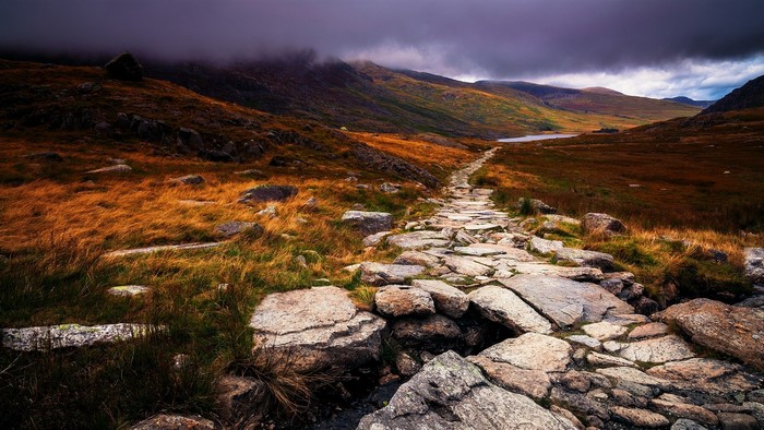Stone path through grassy hills under cloudy sky