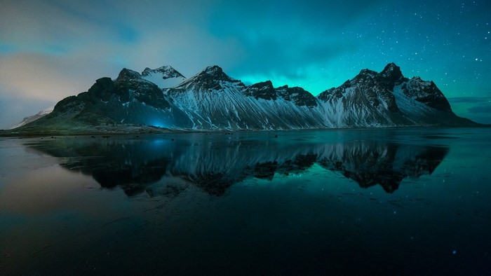 Vestrahorn mountains reflecting in water under aurorae in Iceland