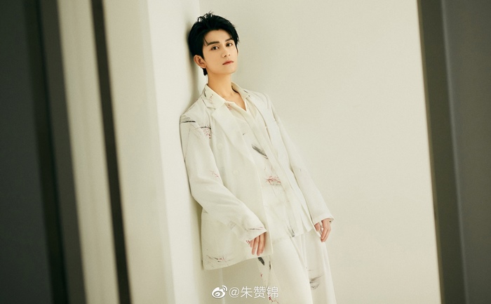 Zhu Zanjin leans against a wall in a white suit