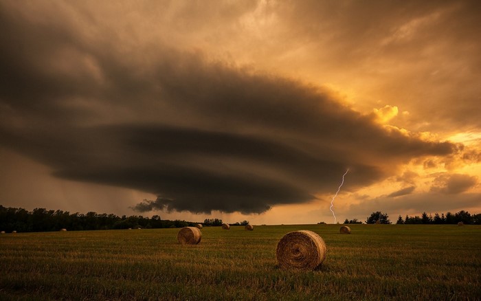 Stormy sky with lightning over a field of hay bales