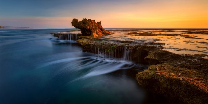 Ocean sunset over rocky coastline with waterfalls
