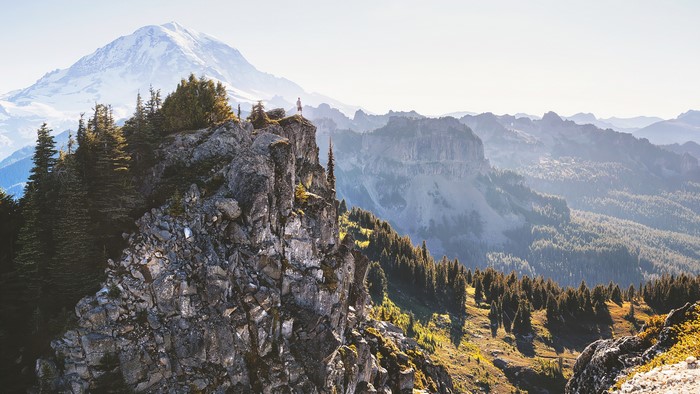 Man standing on a rocky cliff overlooking mountains and forest