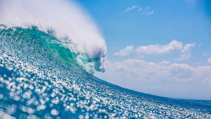 Crashing ocean wave under a blue sky with clouds