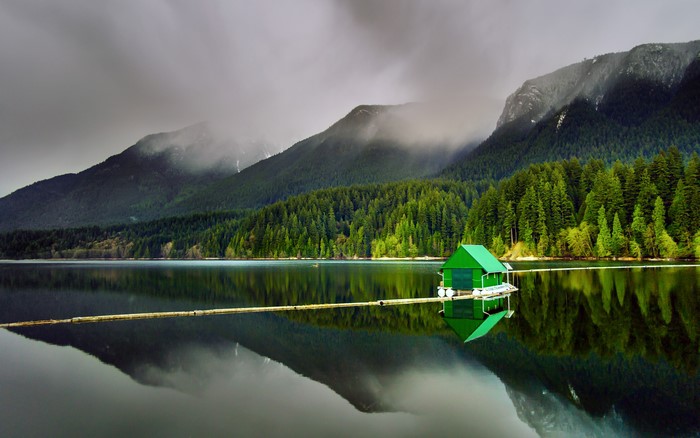 Green boathouse on a calm lake with mountains