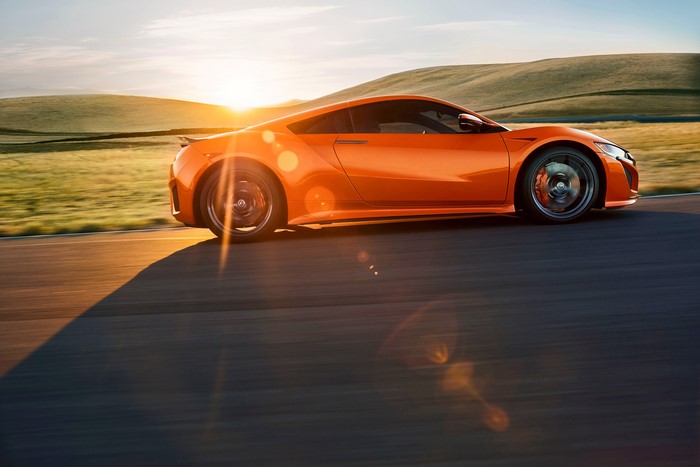 Orange Acura NSX driving on a road at sunset