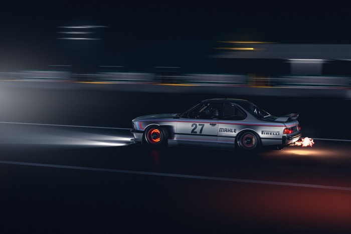 Silver BMW E24 with number 27 on a race track at night