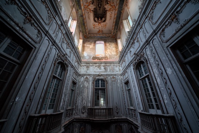 Abandoned ornate interior with peeling paint and tall windows