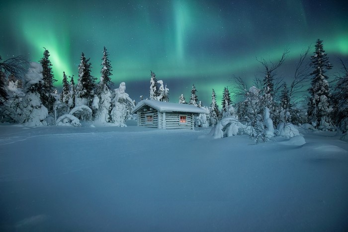Log cabin under aurora borealis in snowy Finland