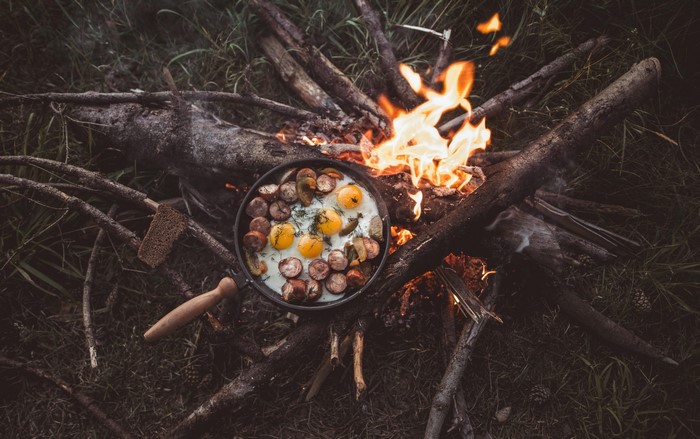 Fried eggs and sausages cooking on a campfire