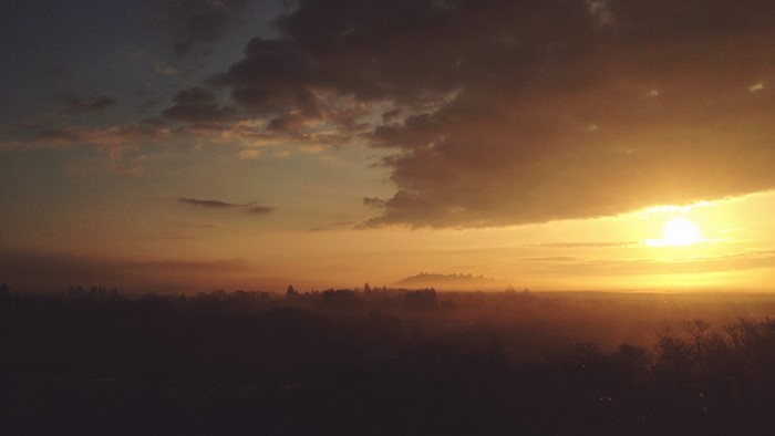 Sunrise over a misty landscape with trees and clouds