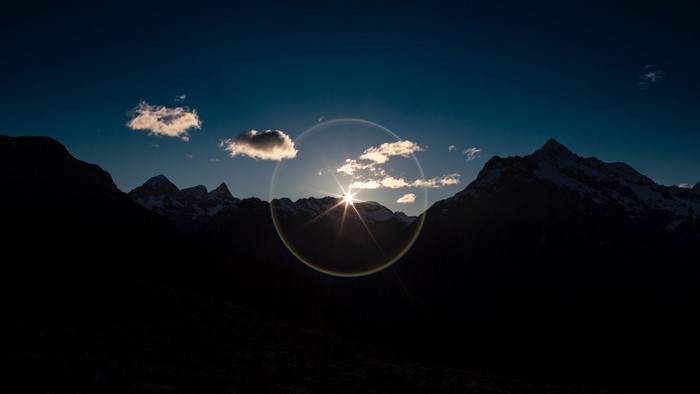 Sun setting behind snow-capped mountains with clouds