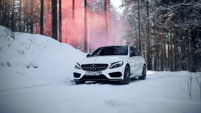 White Mercedes Benz C-Class in snowy forest with red smoke
