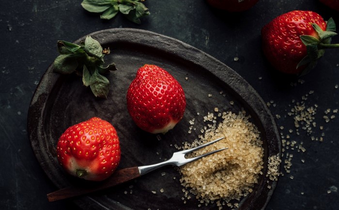 Strawberries with sugar and a fork on a dark plate