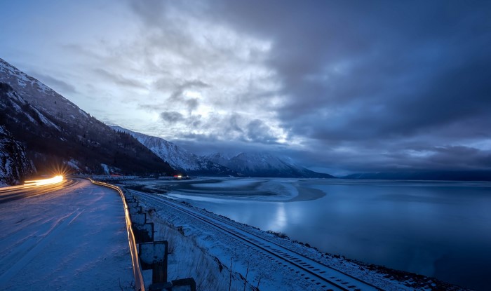 Snowy road and train tracks by a bay at dusk