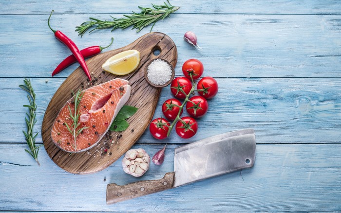 Salmon steak with tomatoes, chili peppers, garlic, and rosemary on a cutting board