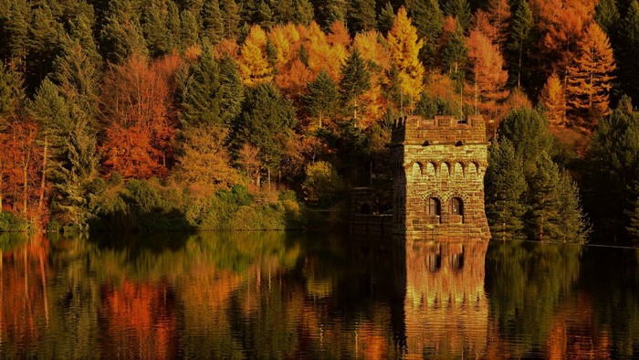 Stone tower in a lake with autumn forest reflection