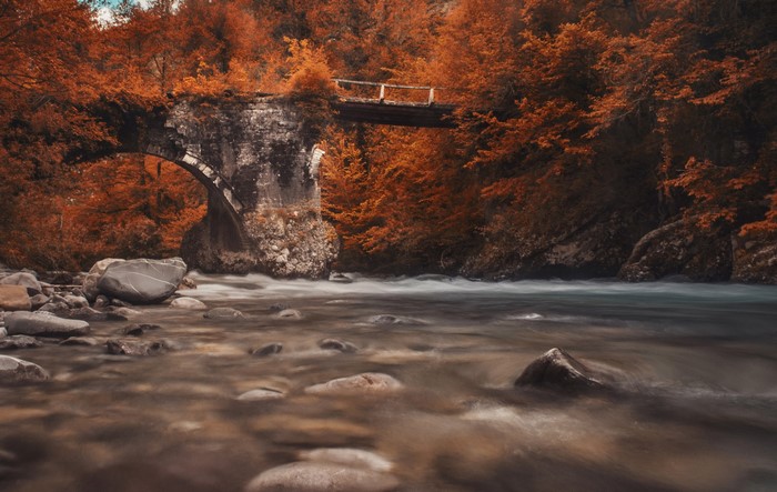 Stone bridge over a river in autumn forest