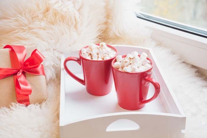 Two mugs of hot chocolate with marshmallows and a gift
