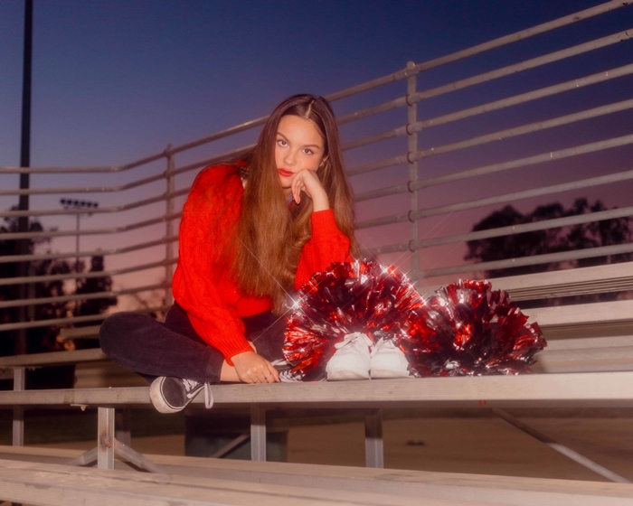 Olivia Rodrigo sitting on bleachers with pom-poms