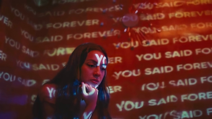 Olivia Rodrigo in a room with "YOU SAID FOREVER" projected