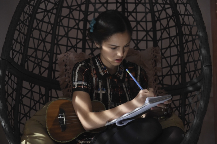 Olivia Rodrigo writing in a notebook with a ukulele