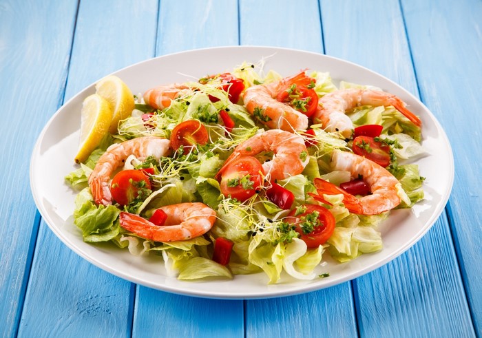 Shrimp salad with tomatoes and lemon on a white plate