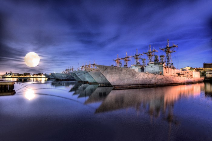 US Navy ships docked at night under a full moon