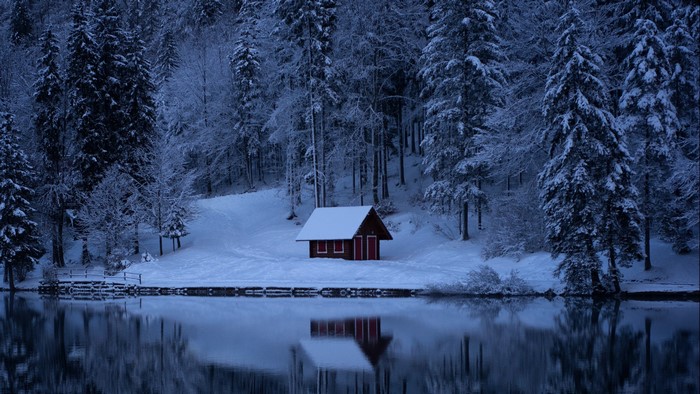 Red cabin by a snowy lake in a winter forest