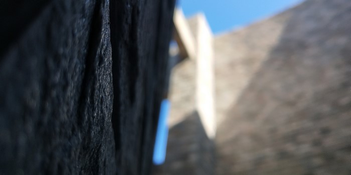 Close-up of textured dark surface with blurred architecture and sky