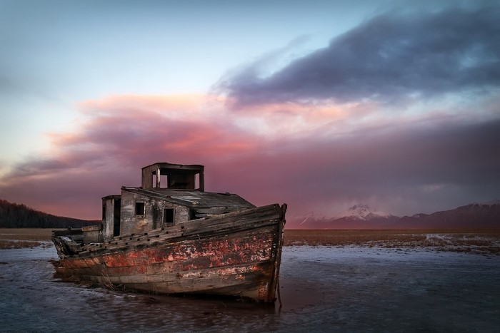 Abandoned wooden boat on frozen ground at sunset