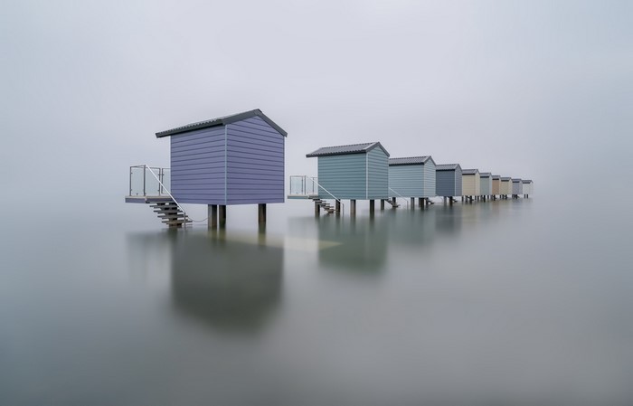 Row of colorful beach huts on stilts in the mist
