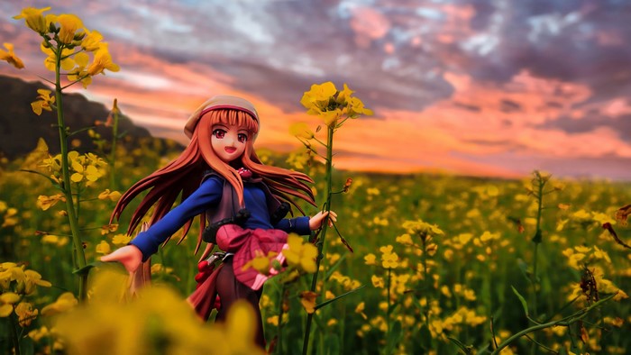 Anime girl figurine in a field of yellow flowers at sunset