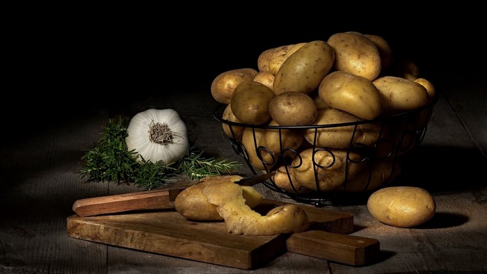 Still life of potatoes, garlic, and rosemary on a cutting board