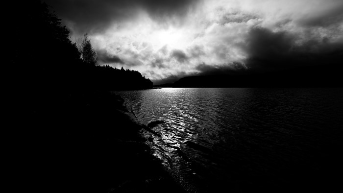 Monochrome landscape of a lake with stormy clouds and sunlight